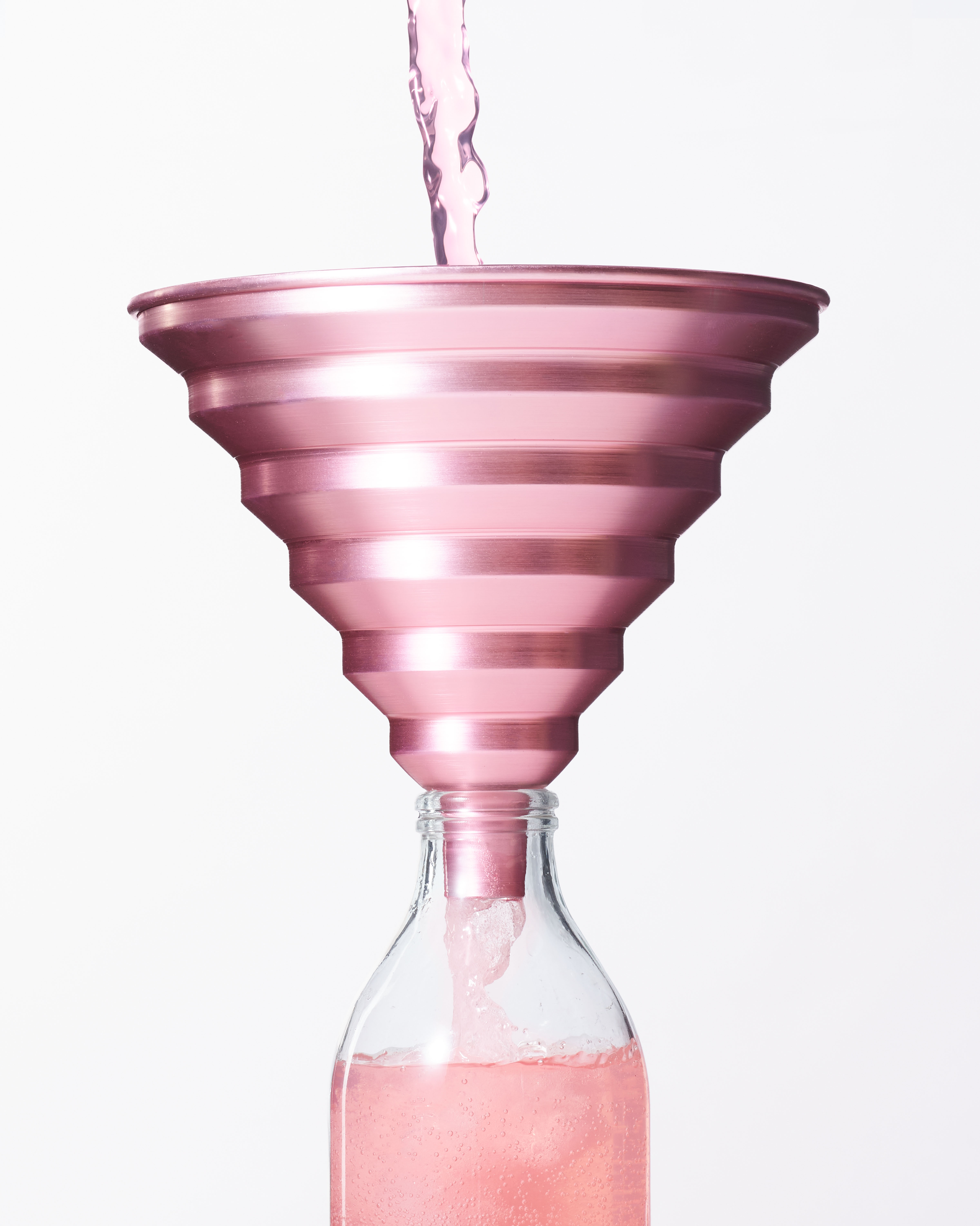 Cropped image of a pink anodised stepped edge aluminium kitchen funnel with pink lemonade being poured through it into a bottle