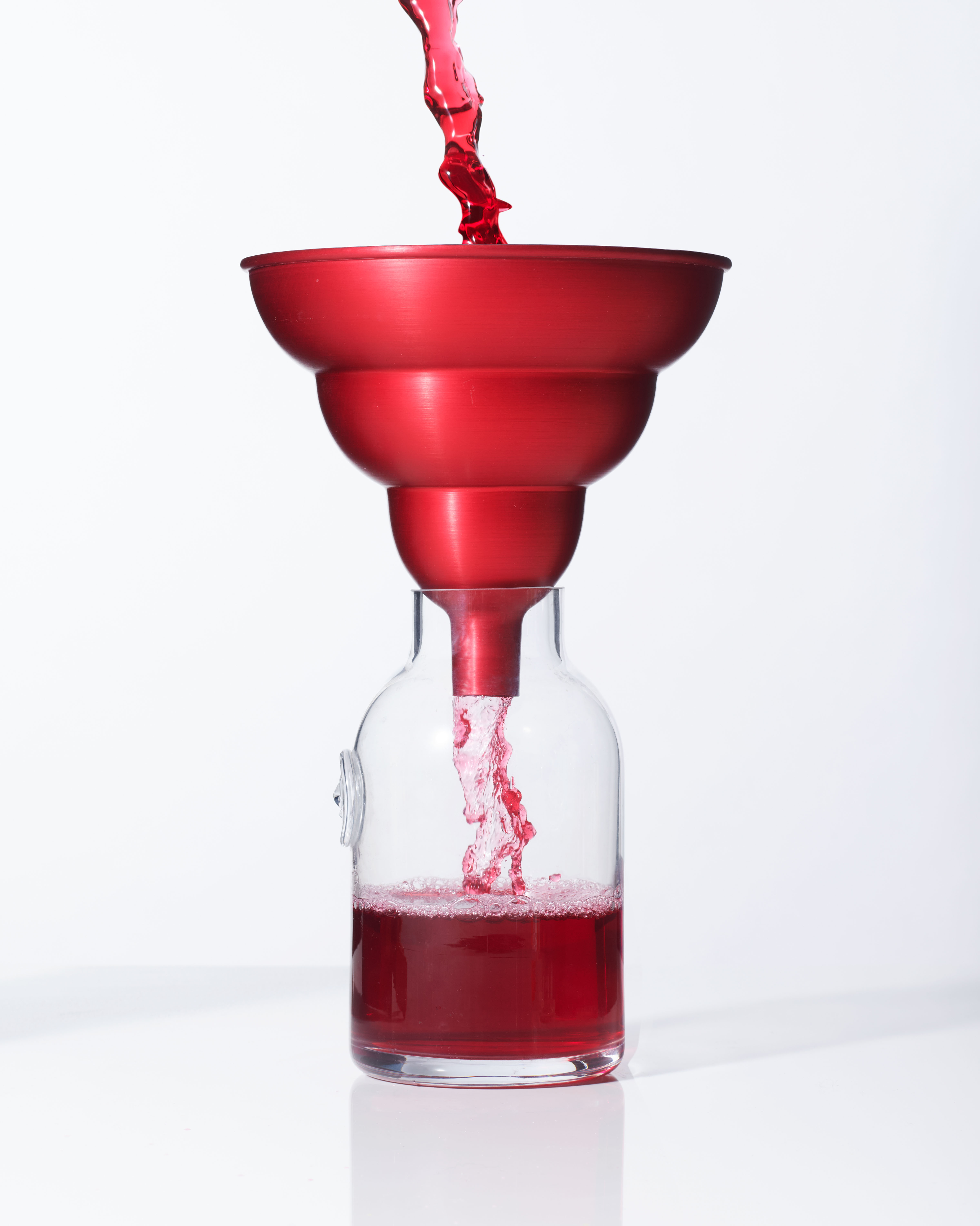 Image of a red anodised grammar phone shaped aluminium kitchen funnel with strawberry cordial being poured through it into a bottle