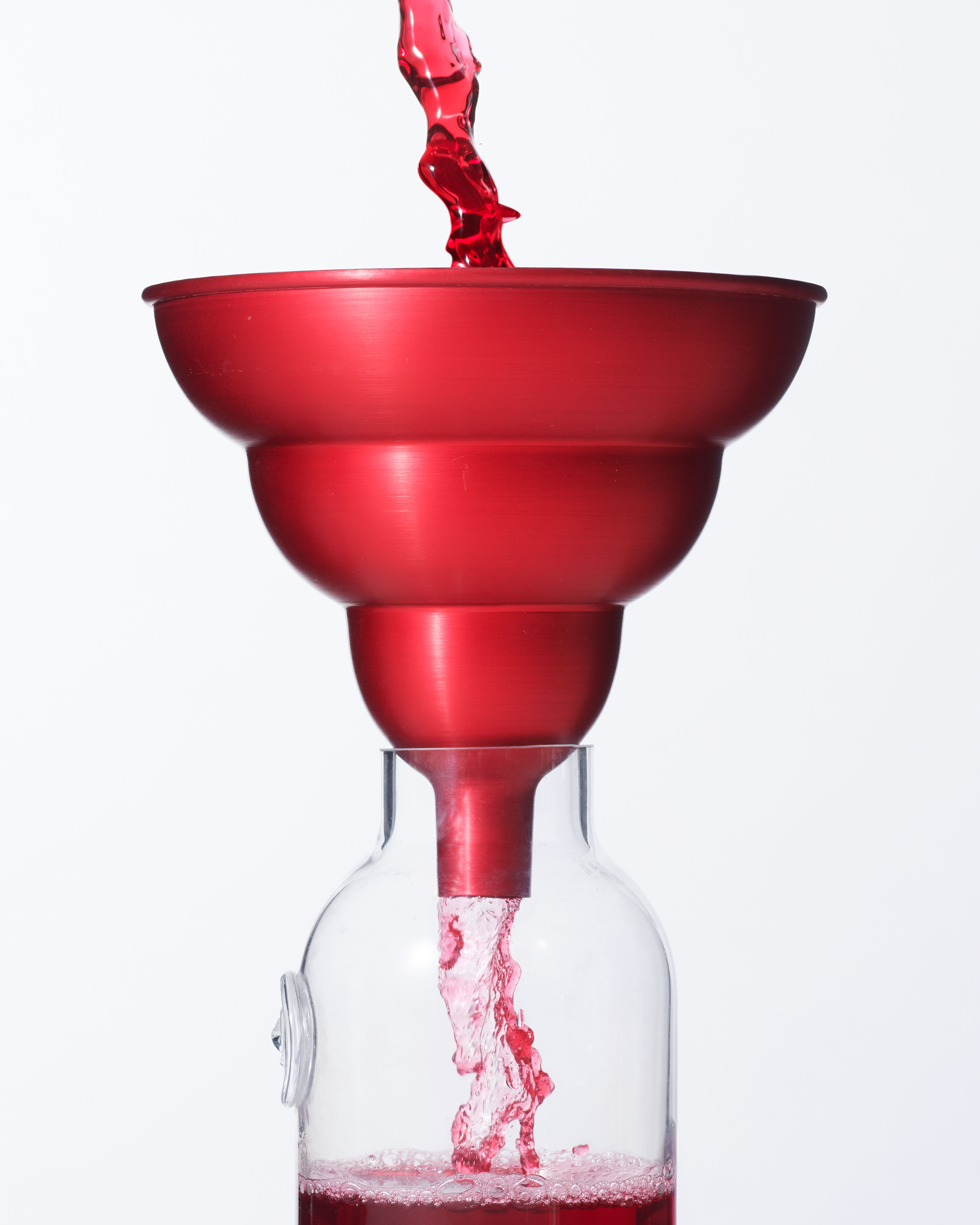 Cropped Image of a rounded, tiered, red anodised aluminium kitchen funnel, with strawberry cordial being poured through it into a bottle