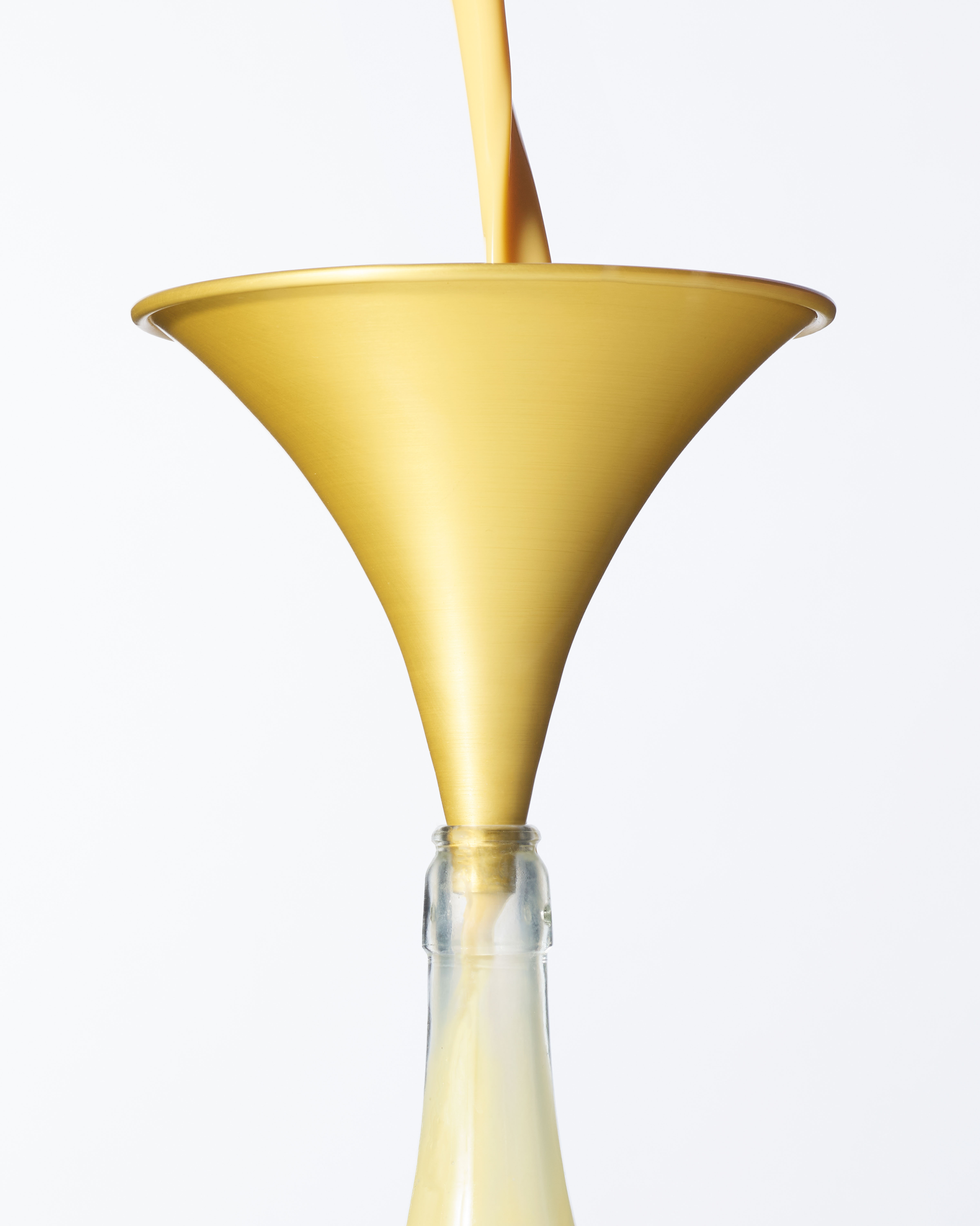 Cropped Image of a yellow anodised aluminium kitchen funnel, reimagined with banana milkshake being poured through it into a bottle